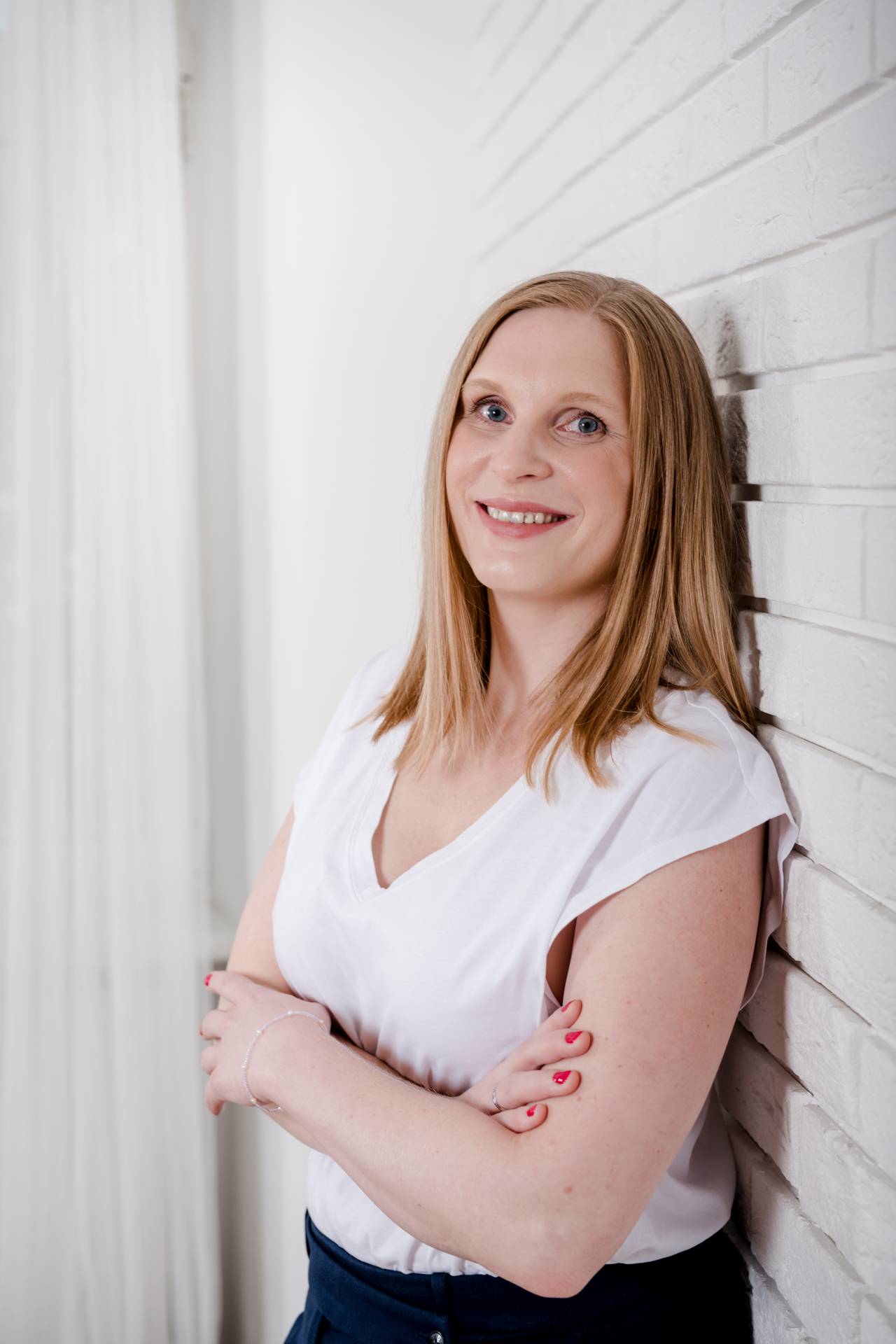 Kathrin Zhuber von DOC-N-ROLL lehnt während eines Business Shootings an einer weißen Ziegelwand.