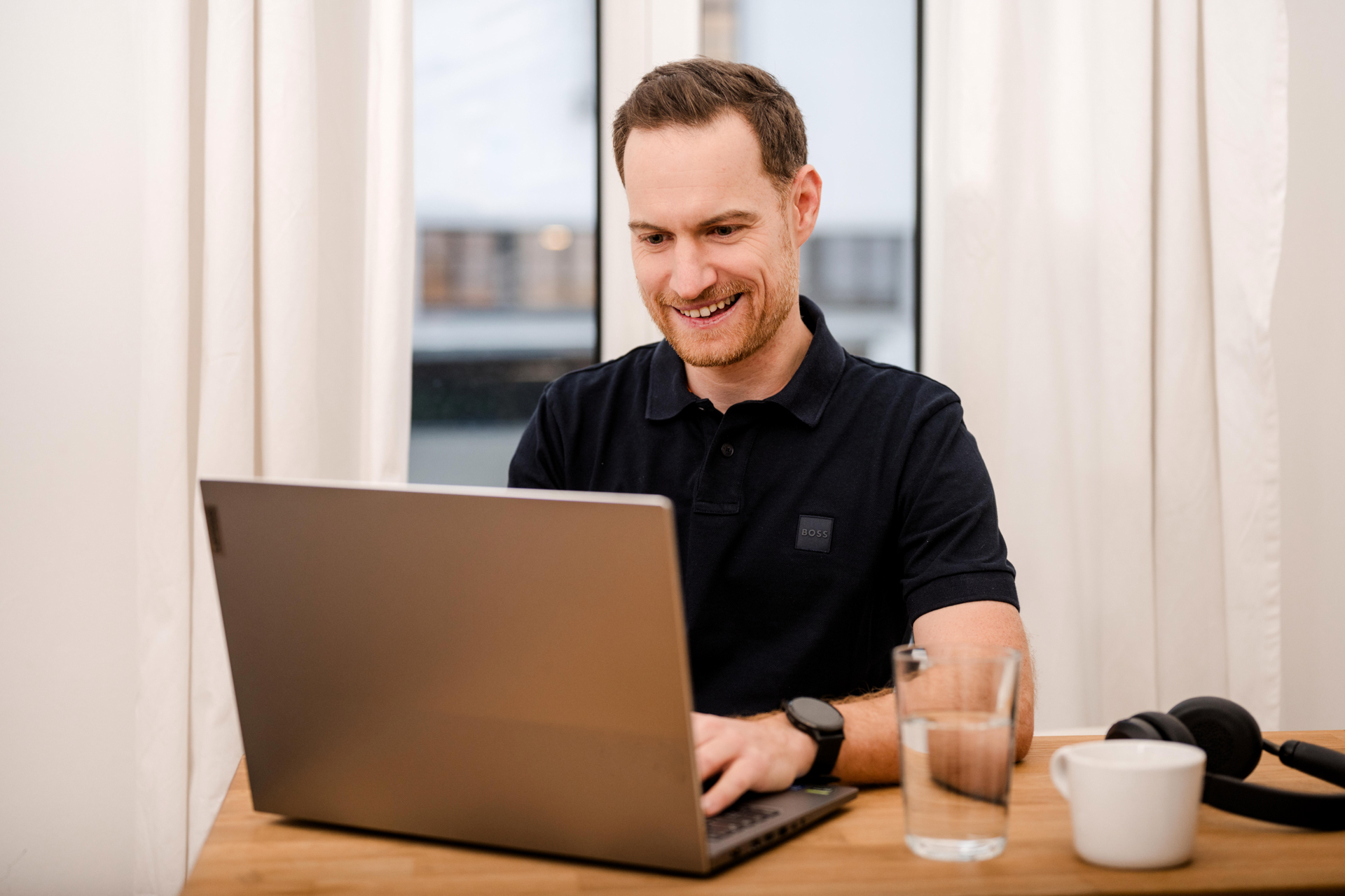 Personal Branding Fotografie Wien: Markus Schick arbeitet konzentriert an seinem Laptop, eine Tasse Tee und ein Glas Wasser stehen auf dem Tisch.