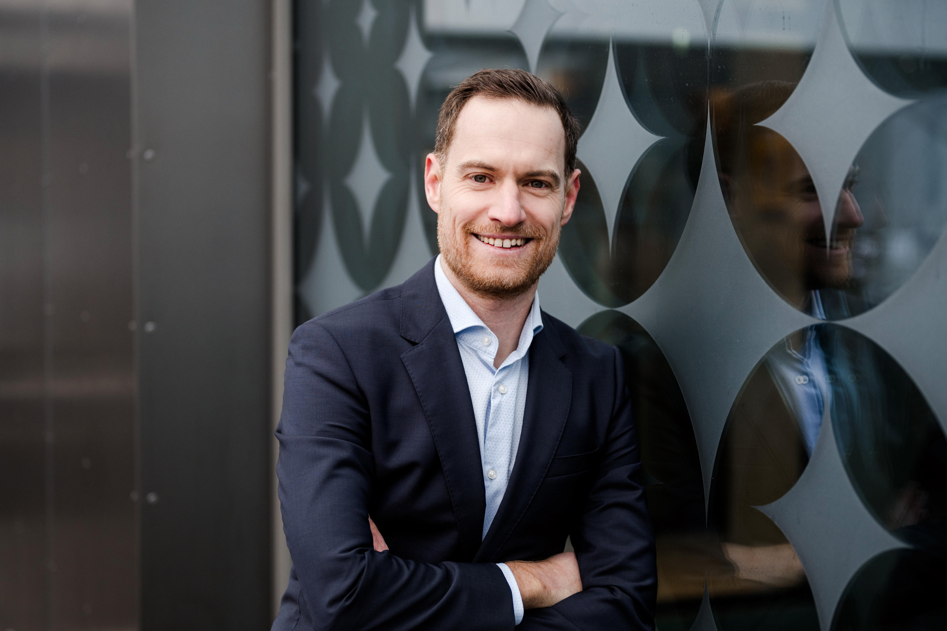 Personal Branding Fotografie Wien: Porträt von Markus Schick (Consulting GmbH) im Anzug, lächelnd vor einer modernen Glasfassade.