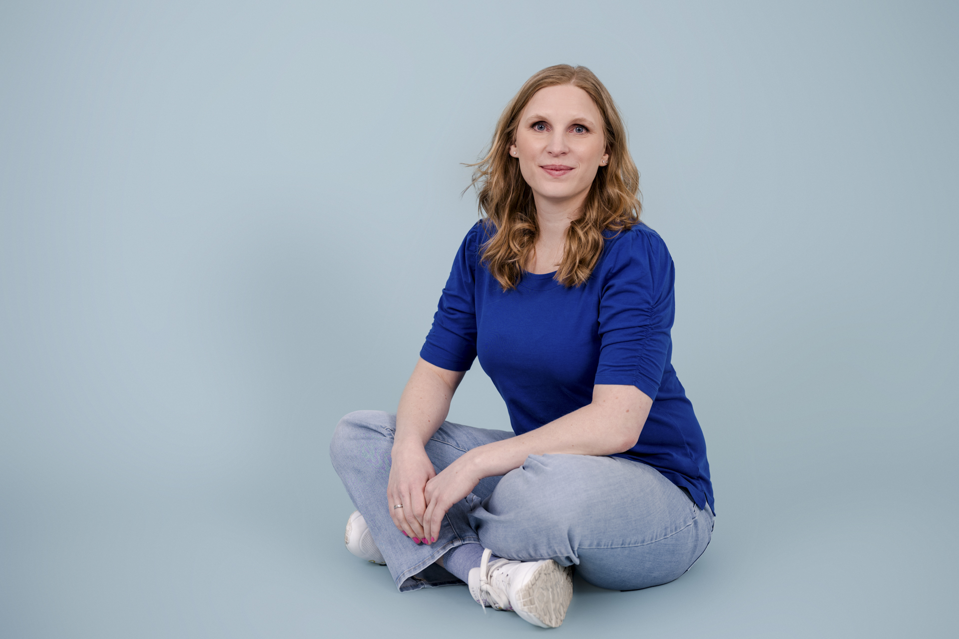 Kathrin Zhuber von DOC-N-ROLL sitzt während eines Personal Branding Shootings auf dem Boden vor hellblauem Hintergrund.