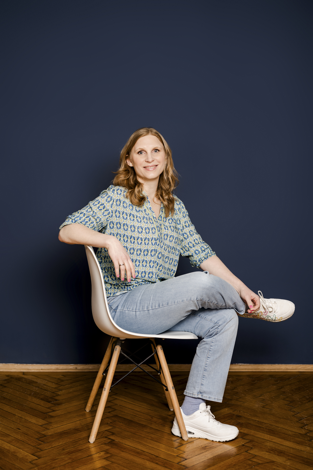Kathrin Zhuber sitzt während eines Personal Branding Shootings auf einem Stuhl vor dunkelblauem Hintergrund.